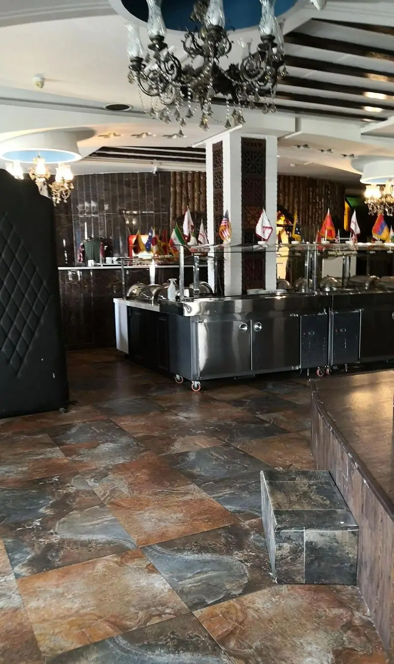 نمای داخلی شیک رستوران شهربانو، بوفه سلف سرویس با میزهای گرم غذا، پرچم‌های بین‌المللی، لوسترهای کلاسیک و کفپوش سنگی مدرن.