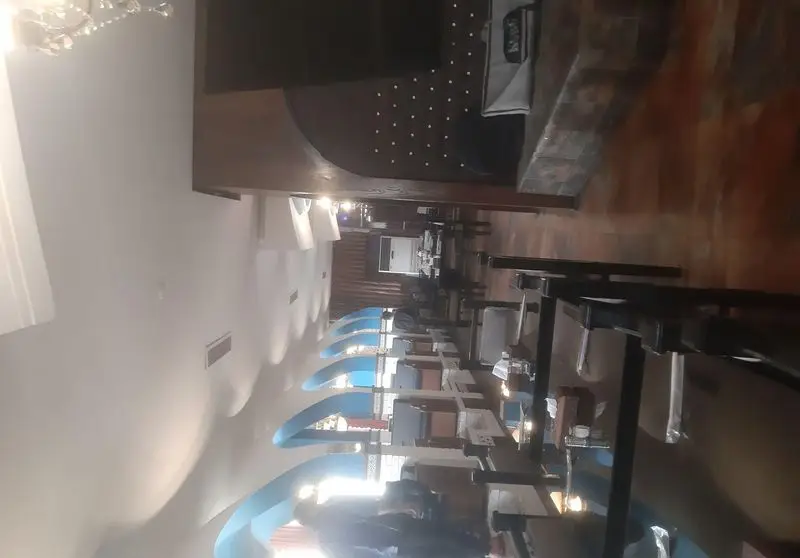 فضای داخلی رستوران شهربانو با طراحی مدرن، میز و صندلی‌های چوبی، دکوراسیون زیبا شامل آرک‌های آبی روشن و نورپردازی گرم برای تجربه‌ای لذت‌بخش.