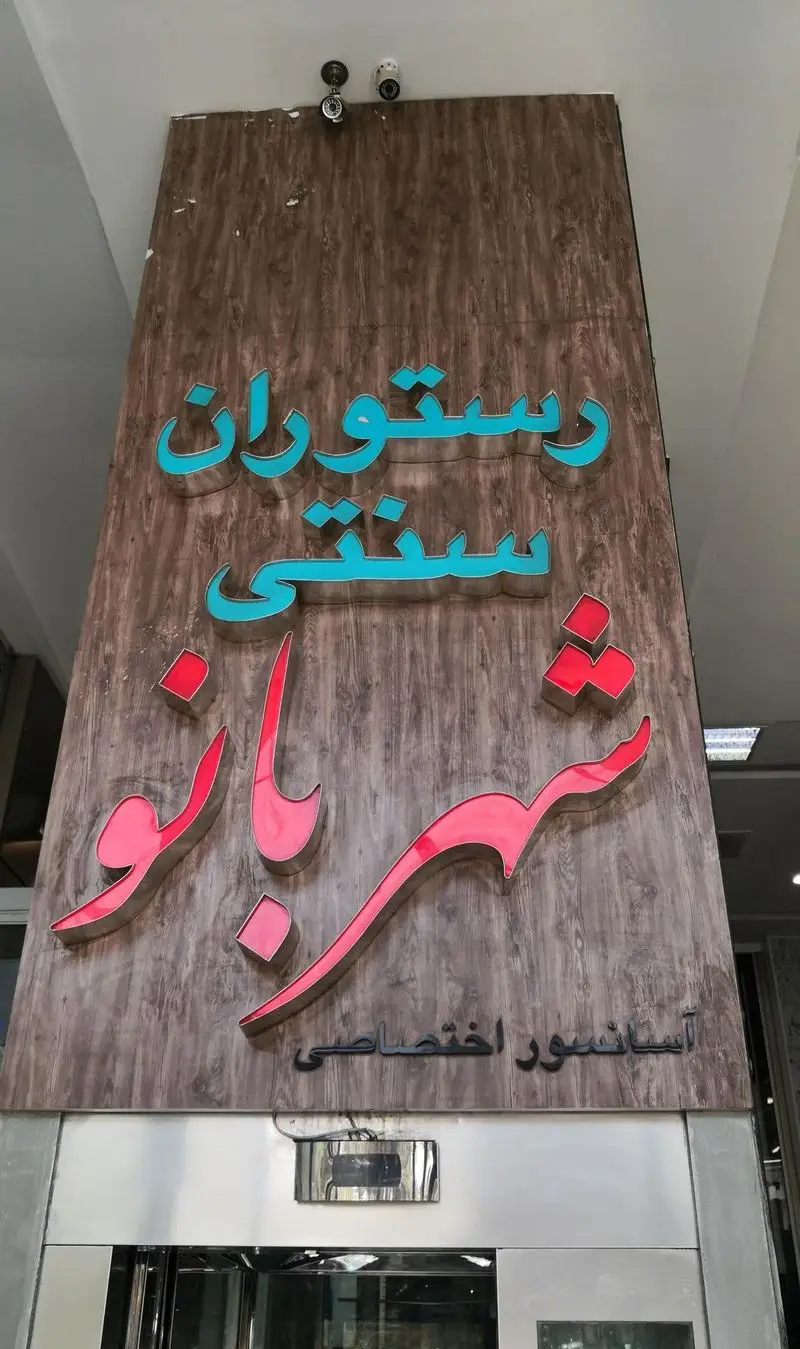 تابلوی بزرگ ورودی رستوران سنتی شهربانو با حروف برجسته آبی و صورتی روی زمینه چوبی. نشان آسانسور اختصاصی.