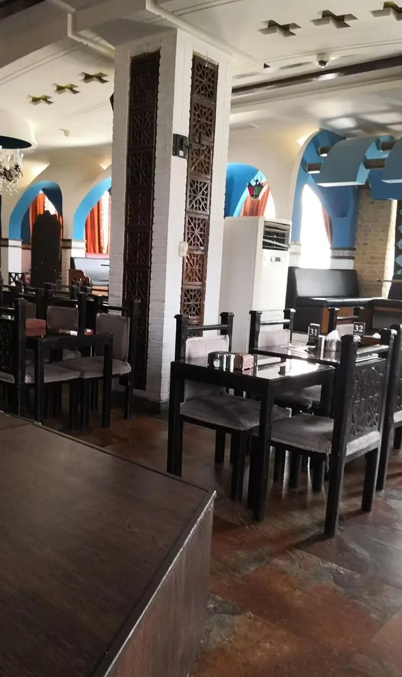 فضای رستوران شهربانو با چیدمان دلپذیر میز و صندلی‌های چوبی، ستون‌های تزئین شده و طاق‌های آبی که فضایی آرامش‌بخش ایجاد کرده است.