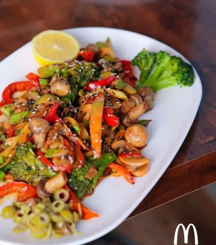 بشقاب سبزیجات تفت داده شده رنگارنگ شامل کلم بروکلی، قارچ و فلفل دلمه‌ای با تزئین کنجد و لیمو؛ غذای سالم از فست فود مادر.