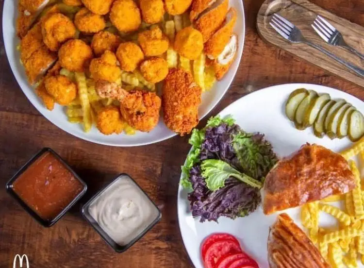 تصویری جذاب از انواع غذاهای فست فود مادر: مرغ سوخاری، ناگت، سیب زمینی سرخ کرده، سالاد تازه و دو نوع سس خوشمزه.