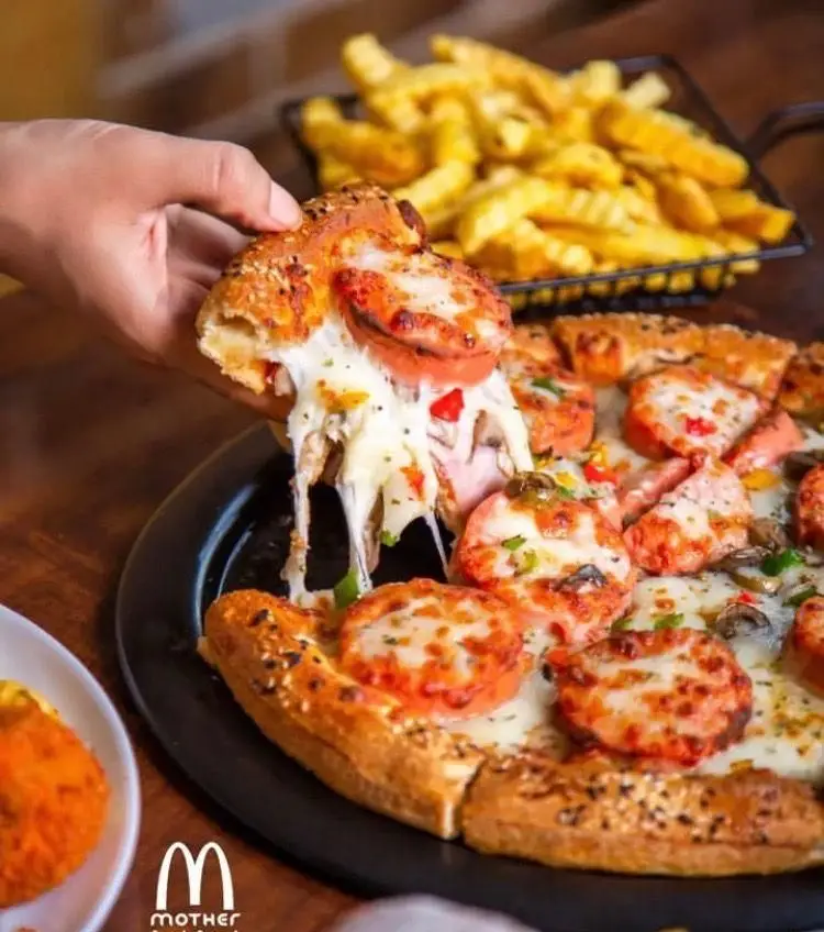 یک اسلایس پیتزای فست فود مادر با پنیر کش‌دار و تاپینگ‌های متنوع، در کنار سیب زمینی سرخ کرده طلایی. لذت یک غذای خوشمزه.