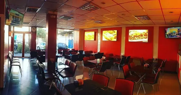 نمای داخلی شیک و مدرن پیتزا غزال با دیوارهای قرمز و میزهای تیره، نمایش‌دهنده غذاهای لذیذ پیتزا، لازانیا و ساندویچ.