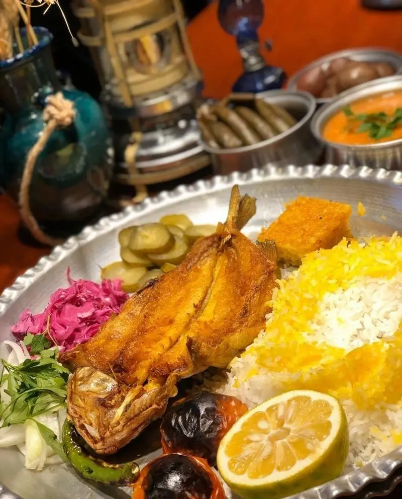 تصویری جذاب از ماهی سرخ شده با پلو زعفرانی، ترشی، سبزیجات تازه و لیمو در رستوران مهدی، نماد غذای اصیل ایرانی.