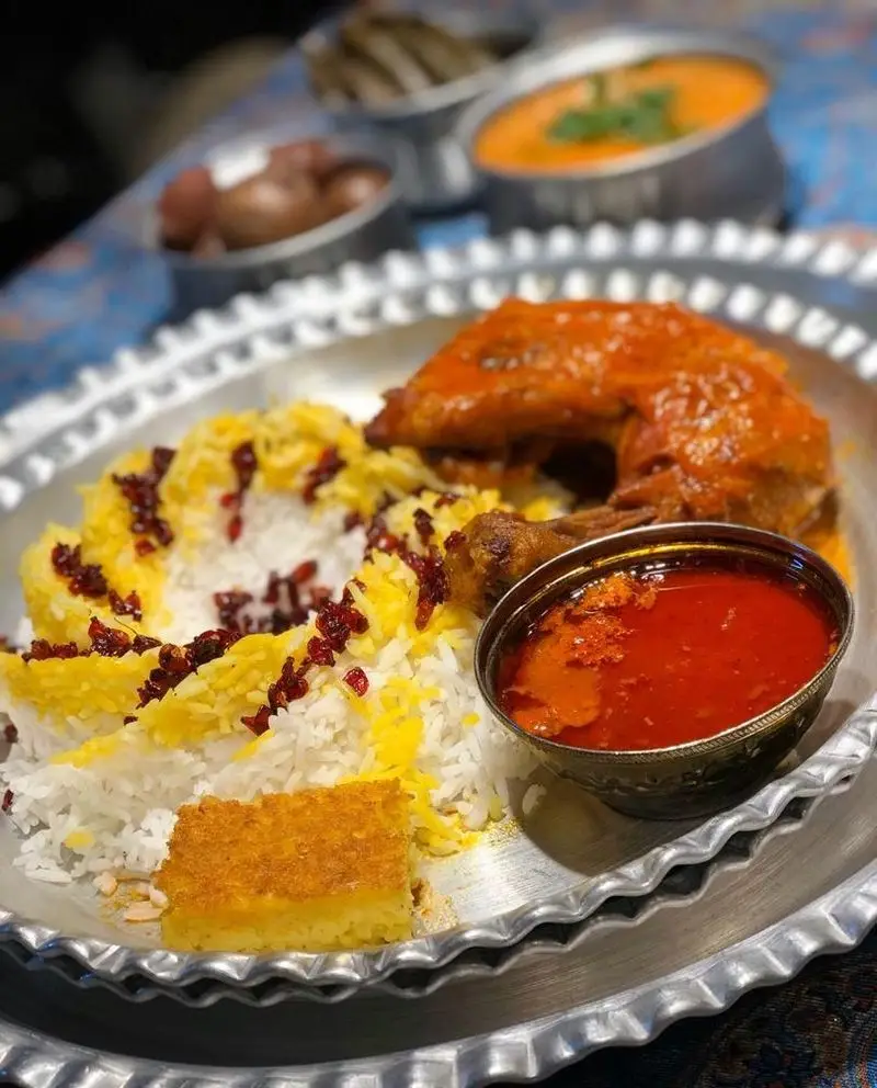 غذای خوشمزه زرشک پلو با مرغ، ته دیگ زعفرانی و خورش در سینی فلزی رستوران مهدی، تجربه‌ای لذت‌بخش از غذای اصیل ایرانی.