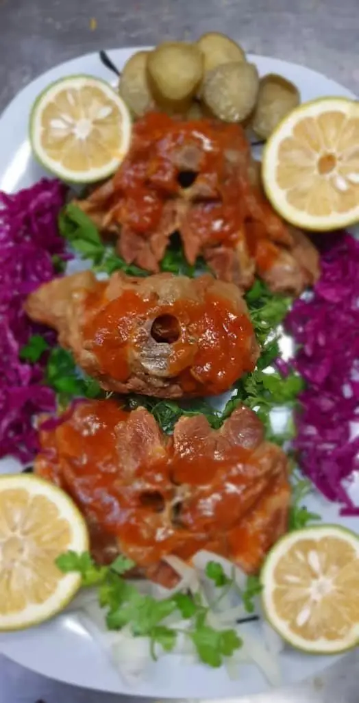 غذای گوشتی لذیذ رستوران مهدی: تکه‌های گوشت با سس قرمز، به همراه لیمو، سبزی، کلم بنفش و سیب‌زمینی. غذایی خوشمزه و اشتهاآور.