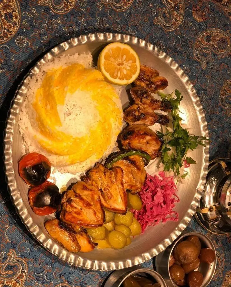 غذای لذیذ ایرانی در رستوران مهدی: جوجه کباب با برنج زعفرانی، گوجه کبابی و انواع ترشی. تجربه طعم اصیل و سنتی.
