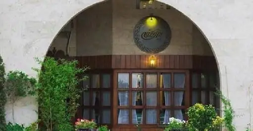 تصویری از نمای بیرونی و ورودی اصلی فست فود بیزی کافه، با سردر سنگی هلالی، در و پنجره‌های چوبی زیبا و تزئینات گیاهان سبز.