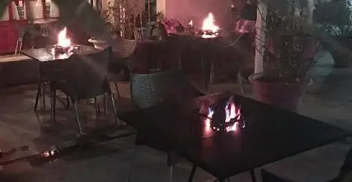 فضای باز دلنشین و دنج فست فود بیزی کافه در شب با میز و صندلی و شعله‌های آتش برای گرمای دلپذیر مشتریان.