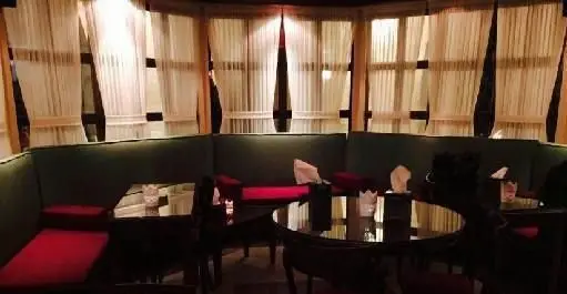 فضای داخلی دنج و شیک فست فود بیزی کافه با مبلمان سبز و قرمز، میزهای تیره و پنجره‌های پرده‌دار. محیطی عالی برای لذت بردن از غذا.