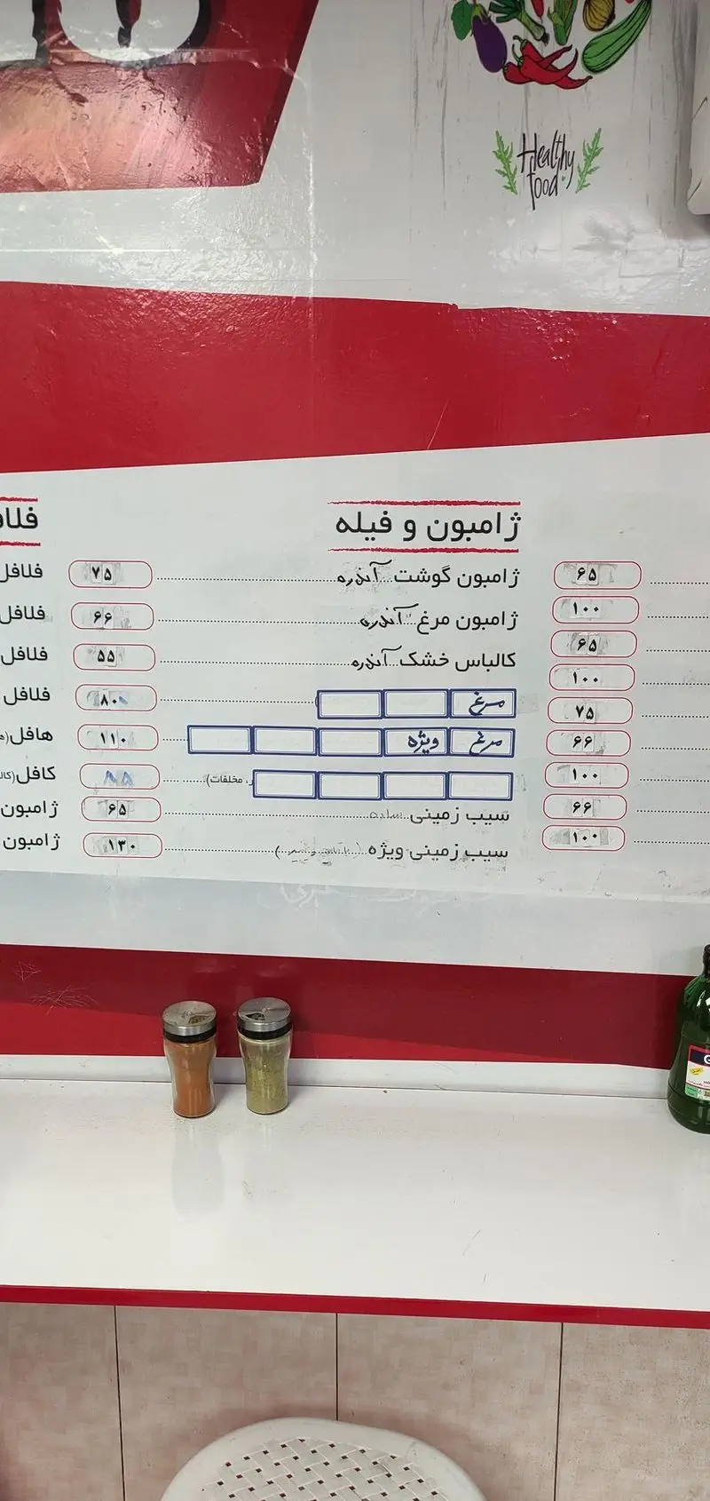 منو دیجیتالی فلافل و ساندویچ منصور با انواع ژامبون، فیله، فلافل و سیب‌زمینی، همراه با قیمت‌ها و ادویه‌ها روی کانتر.