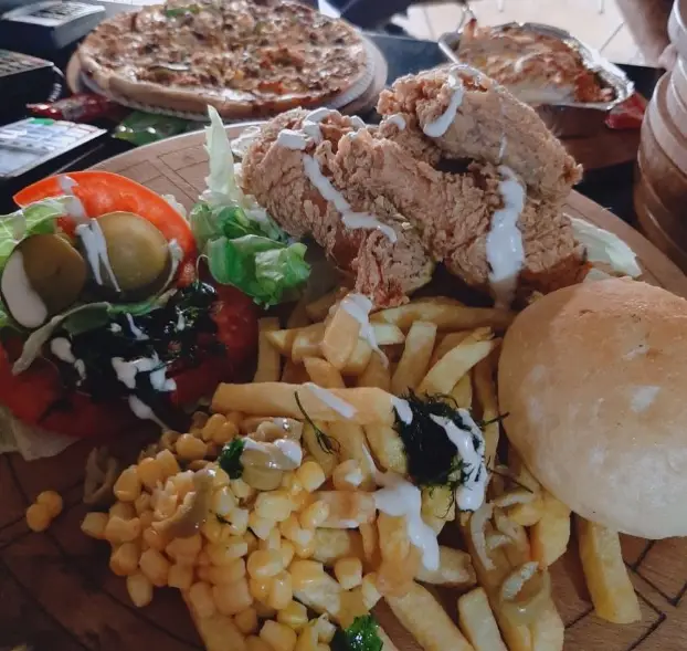 سفره‌ای از غذاهای خوشمزه فست فود بلوط شامل مرغ سوخاری ترد، سیب‌زمینی، ذرت، سالاد و پیتزا. تجربه‌ی یک وعده غذایی لذیذ.