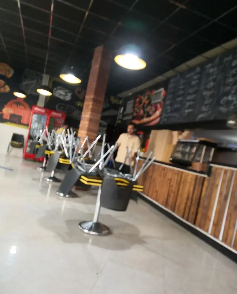 فضای داخلی فست فود بلوط با صندلی های چیده شده روی میزها، دیوارنوشته های پیتزا، یخچال های کوکاکولا و دکوراسیون مدرن