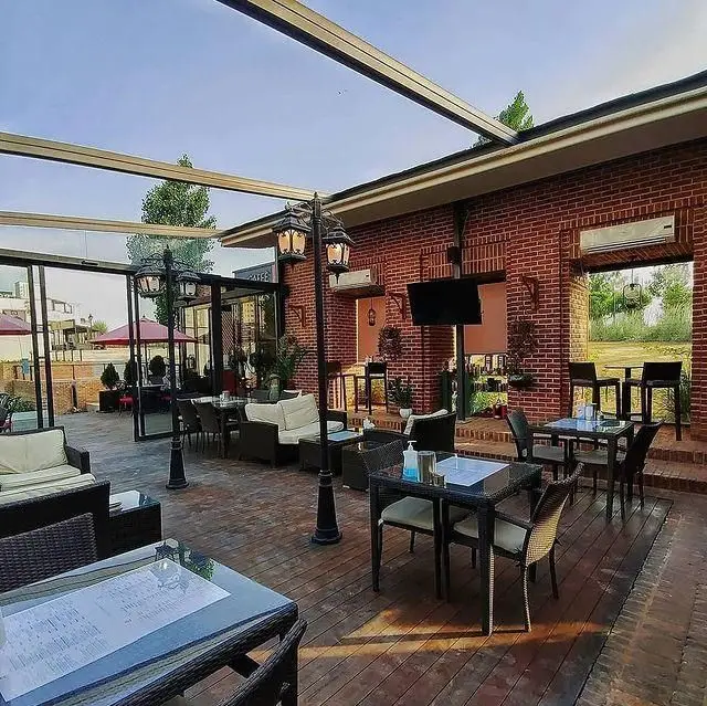 فضای باز و دنج ایلی کافه با میز و صندلی‌های شیک، مبلمان راحتی و دکوراسیون زیبای آجرنما، مکانی ایده‌آل برای استراحت و صرف نوشیدنی.