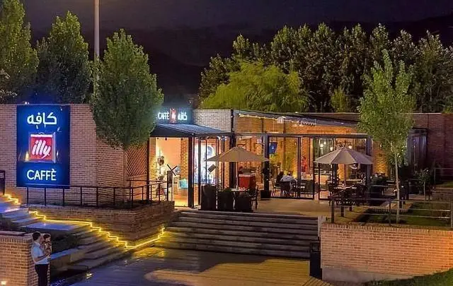 نمایی دلنشین از ایلی کافه در شب با فضای باز، میز و صندلی، و نورپردازی زیبا. بهترین مکان برای تجربه قهوه اصیل.