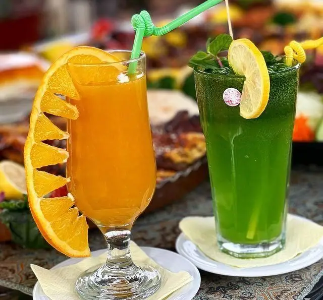 نوشیدنی‌های تازه و خنک باغ رستوران طبیعت: آب پرتقال طبیعی با تزئین پرتقال و شربت نعناع-لیمو با برگ نعناع و لیمو.