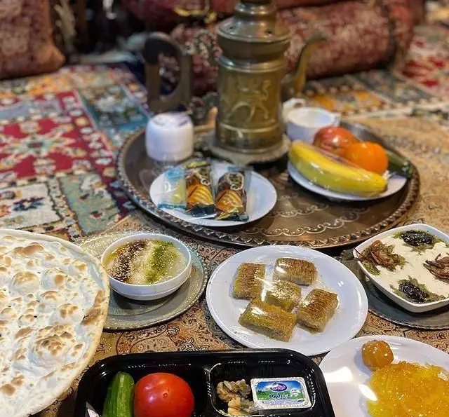 وعده غذایی سنتی و اصیل ایرانی شامل چای، نان تازه، شیرینی، میوه و خوراکی‌های محلی در باغ رستوران طبیعت.