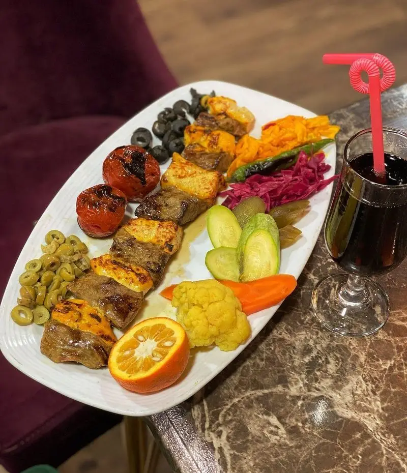 بشقاب لذیذ کباب میکس (چنجه و جوجه) با گوجه کبابی، زیتون، ترشیجات (خیار، کلم، هویج، گل کلم) و نوشیدنی در باغ رستوران طبیعت.