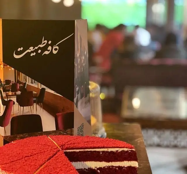 کیک ردولوت خوشمزه و برش‌خورده روی میز در کافه طبیعت، فضایی دنج و دلنشین در باغ رستوران طبیعت برای دورهمی.