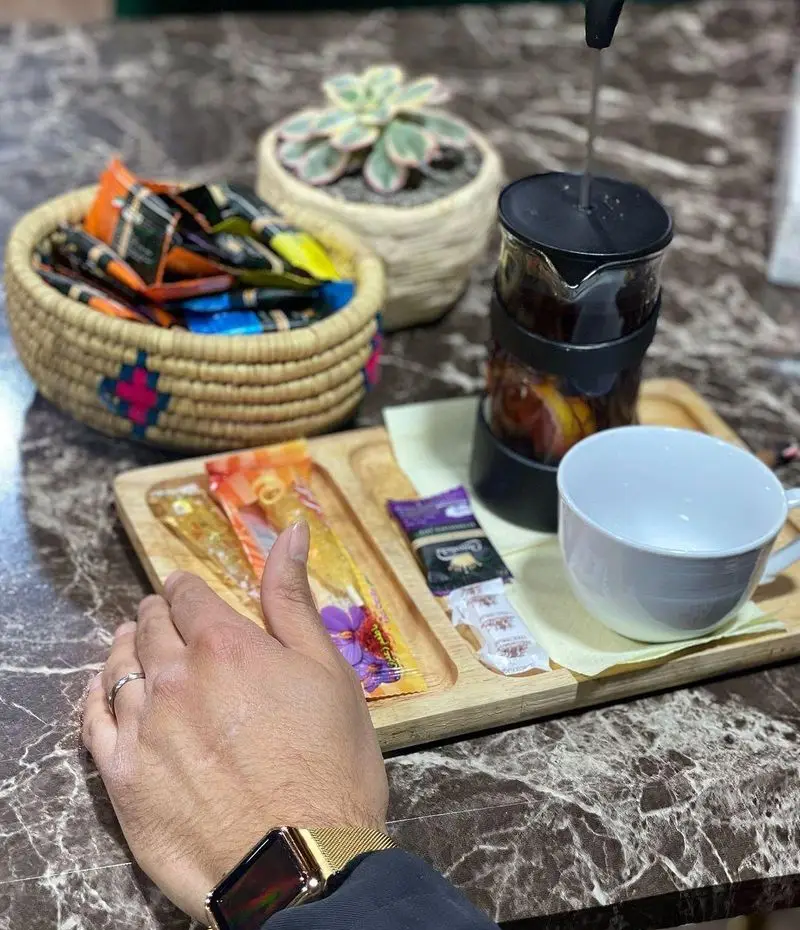 تجربه دلنشین نوشیدن دمنوش و چای تازه در فضای آرام و سبز باغ رستوران طبیعت. سینی چوبی با عسل و شکر، فرنچ پرس و سبد متنوع چای.