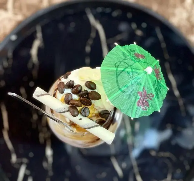 دسر دلپذیر و نوشیدنی سرد در باغ رستوران طبیعت، تزئین شده با بستنی، دانه‌های قهوه تازه، ویفر و چتر کوچک.