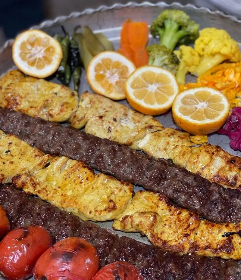 مجموعه‌ای از کباب کوبیده و جوجه کباب اصیل و لذیذ باغ رستوران طبیعت، به همراه گوجه کبابی، لیمو و سبزیجات متنوع.