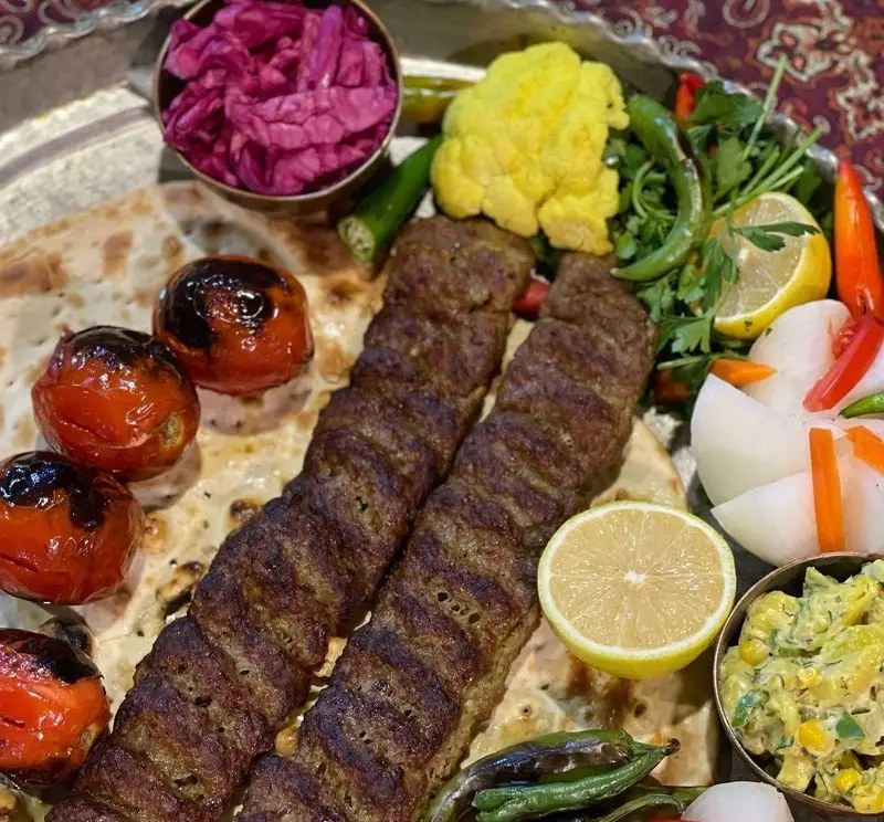 کباب کوبیده لذیذ باغ رستوران طبیعت با نان تازه، گوجه کبابی، لیموترش و مخلفات متنوع ایرانی. تجربه طعم اصیل در طبیعت.