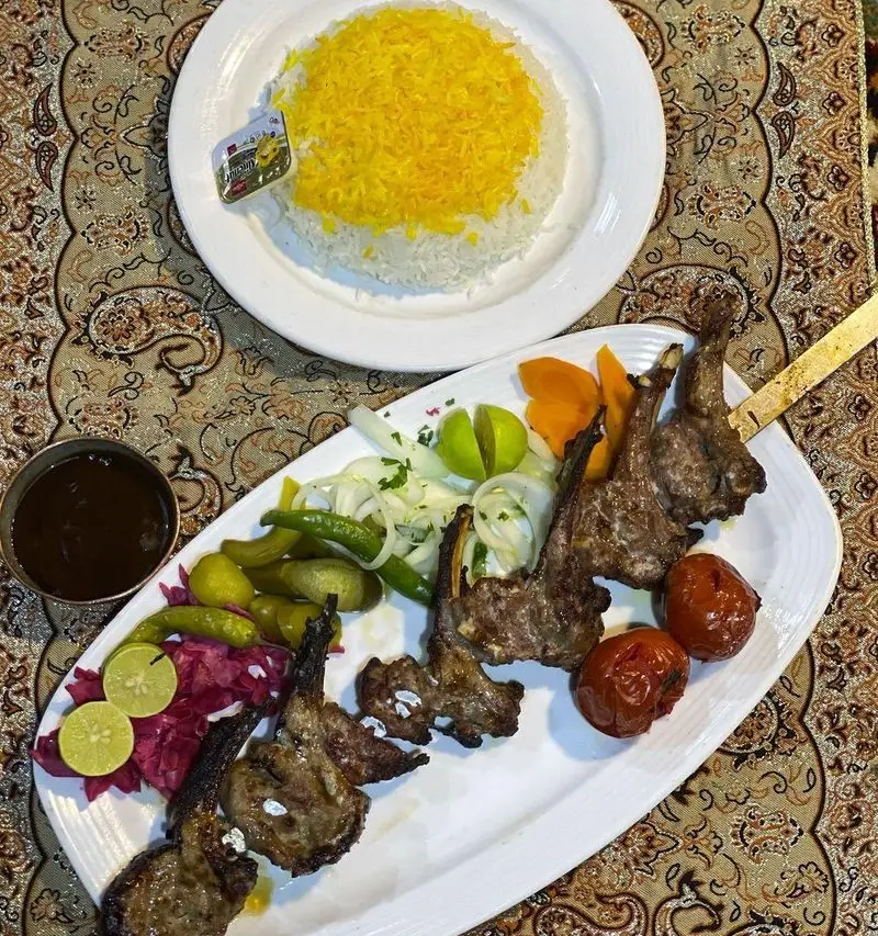 شیشلیک لذیذ باغ رستوران طبیعت با برنج زعفرانی، گوجه کبابی و دورچین تازه. تجربه غذای اصیل ایرانی را با ما داشته باشید.