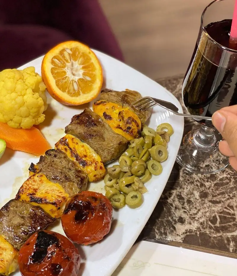 تصویری از کباب مخلوط گوشت و مرغ با گوجه کبابی، زیتون و دورچین رنگارنگ در محیط دلنشین باغ رستوران طبیعت.