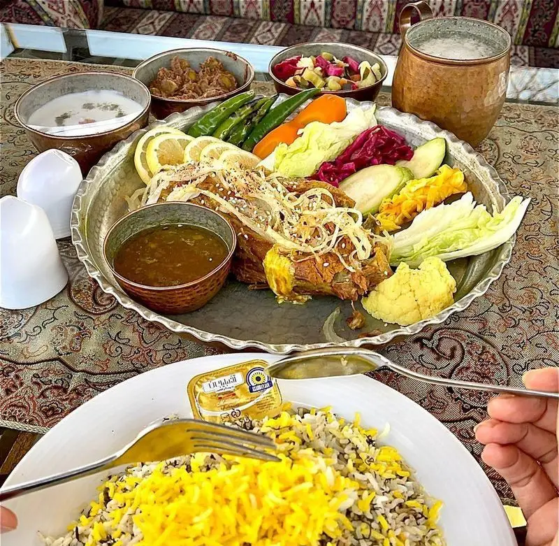 میز غذای اصیل و کامل ایرانی در باغ رستوران طبیعت، شامل پلو، گوشت، خورش، ترشی، سبزیجات تازه و دوغ محلی. تجربه‌ای دلنشین.