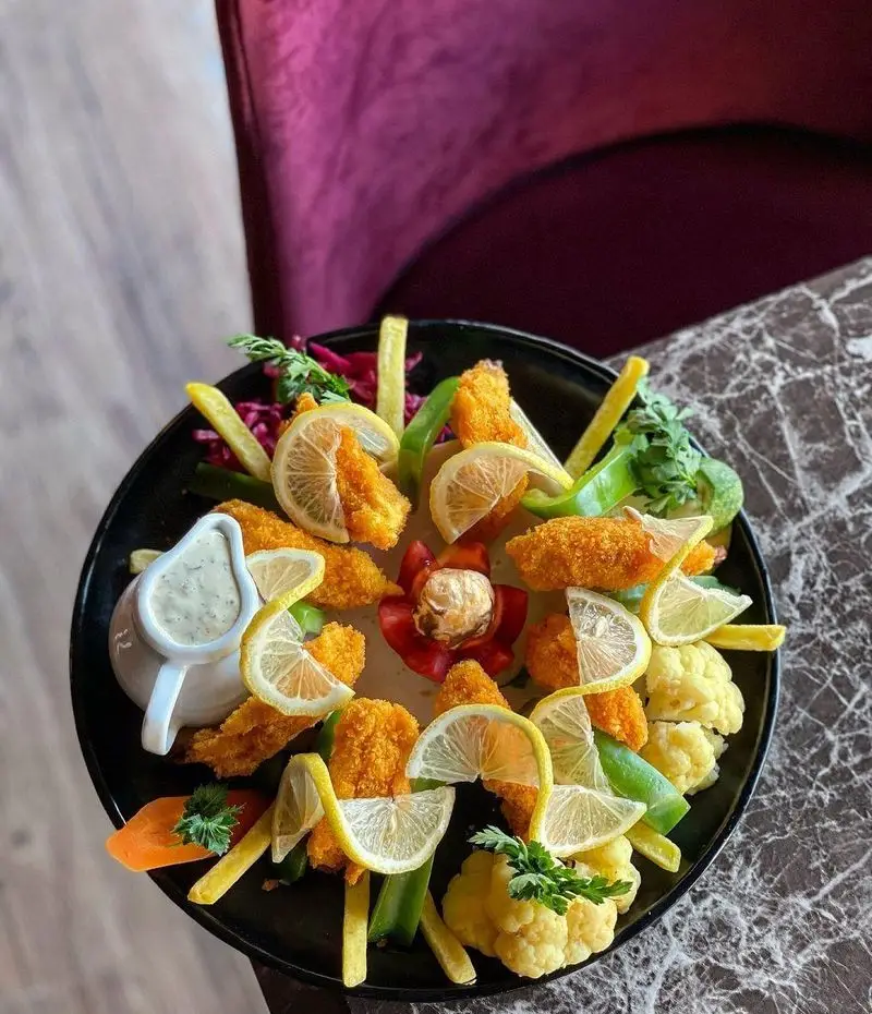 غذای خوشمزه: پلاتر ناگت مرغ کریسپی و طلایی با دورچین سبزیجات تازه، لیمو و سس مخصوص در فضای دلنشین باغ رستوران طبیعت.