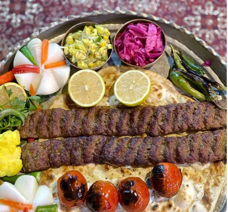 سینی کباب کوبیده مخصوص با نان تازه، گوجه کبابی، لیمو و مخلفات خوشرنگ در باغ رستوران طبیعت، طعم بی‌نظیر غذای ایرانی.