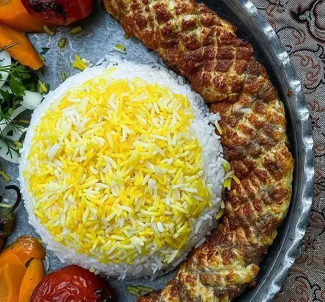 تصویری اشتهاآور از چلو کباب مخصوص باغ رستوران طبیعت با برنج زعفرانی معطر، گوجه کبابی و سبزیجات تازه، نمادی از غذای اصیل ایرانی.
