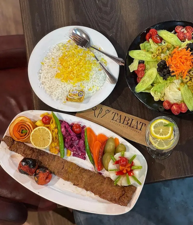 سفره ای دلنشین از کباب کوبیده، چلو زعفرانی، سالاد فصل و مخلفات رنگارنگ در محیط زیبای باغ رستوران طبیعت.