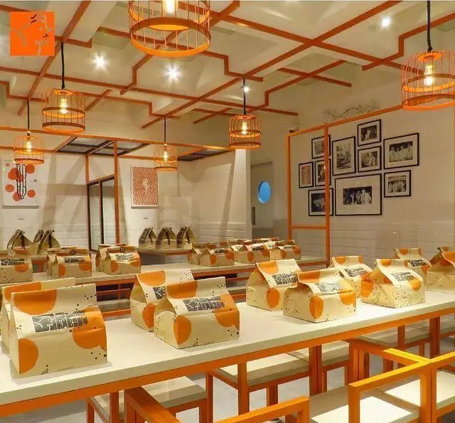 فضای داخلی خاص و مدرن مرغ سوخاری کابوکی، بسته‌بندی‌های نارنجی روی میزها، سقف با دکوراتیو هندسی و قاب عکس‌های دیواری.