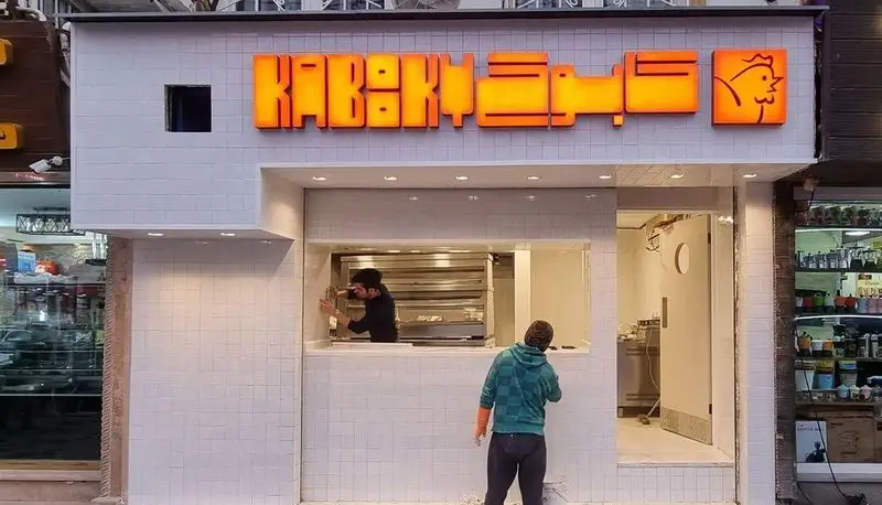 نمای جلویی کسب و کار مرغ سوخاری کابوکی با تابلوی نئون درخشان شامل نام KABUKI و لوگوی مرغ. طراحی جدید و مدرن این فست فود با کاشی‌های سفید.