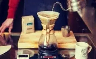 تصویر باریستا در حال دم آوری قهوه دمی با استفاده از کمکس و کتری باریستا در فضای کسب و کار قهوه ساوا. آماده سازی قهوه با ابزار تخصصی.