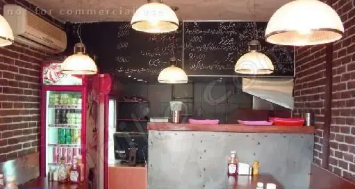 نمایی از دکوراسیون داخلی رستوران دکان برگر، شامل دیوارهای آجری، منوی نوشته شده روی تخته سیاه، پیشخوان و یخچال نوشیدنی.