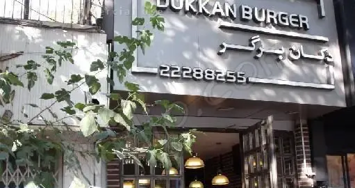 نمایی بیرونی از رستوران دکان برگر، متخصص در همبرگرهای لذیذ و فست فود. تابلو دکان برگر به فارسی و انگلیسی قابل مشاهده است.