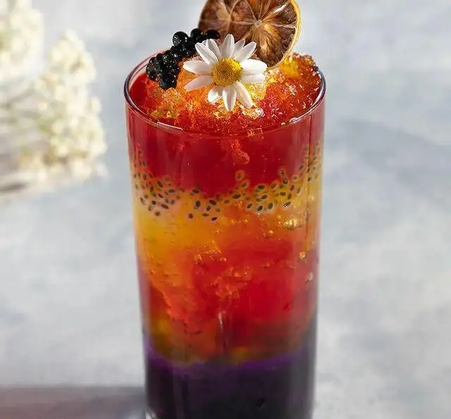 نوشیدنی رنگارنگ لایه ای و خنک از کافه رستوران مگریز، با دانه های تخم شربتی، گل بابونه و لیمو خشک تزئین شده.