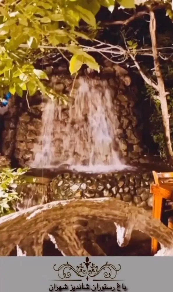 فضای دلنشین باغ رستوران شاندیز شهران تهران با آبشار سنگی جذاب و محیط طبیعی سرسبز برای تجربه غذایی لذت‌بخش.