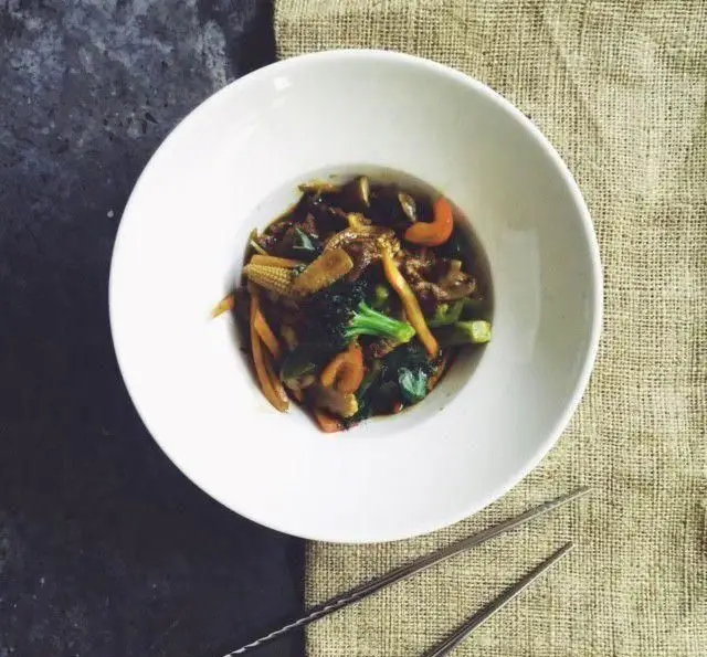 غذای تازه و سالم رستوران واسابی: استیر فرای سبزیجات (بروکلی، هویج، بیبی کورن) و گوشت در سس لذیذ آسیایی، سرو شده با چاپستیک.