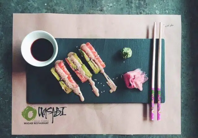 سوشی‌های لذیذ رستوران واسابی؛ رول‌های سالمون و آواکادو با سس، واسابی تازه، زنجبیل و سس سویا. انتخابی عالی برای غذای آسیایی.