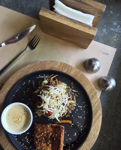 نمایی از یک وعده غذایی لذیذ در رستوران واسابی شامل سالمون گریل با سس کنجد، سالاد سبزیجات و جوانه‌ها روی میز غذاخوری.