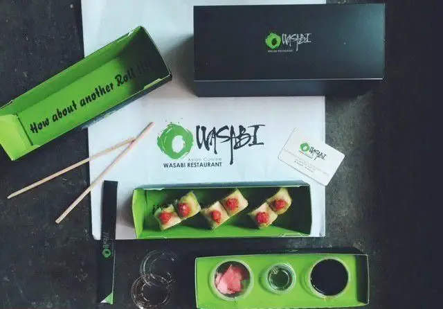 بسته‌بندی شیک و کامل غذای بیرون‌بر رستوران واسابی: سوشی، چاپستیک، سس و مخلفات در جعبه‌های سبز با برند Wasabi. تجربه غذای آسیایی.