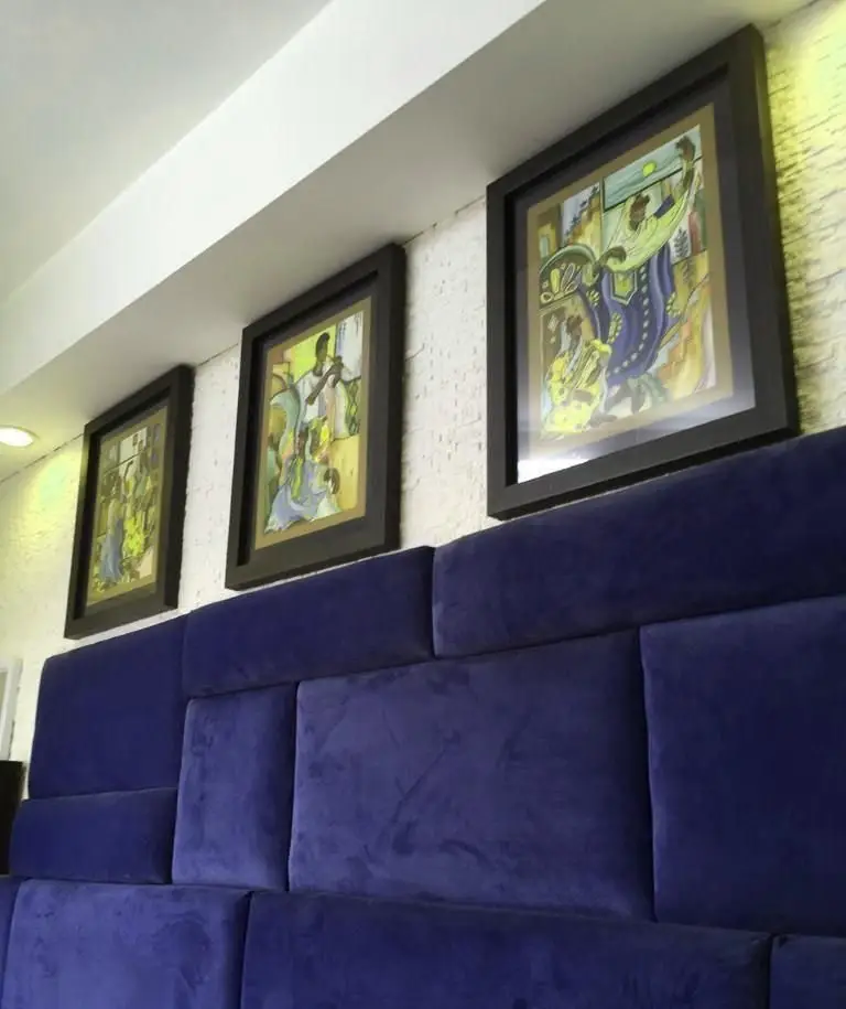 دکوراسیون داخلی شیک ساندویچ ترخون: سه تابلوی نقاشی رنگارنگ بالای دیوارپوش مخملی آبی سلطنتی، فضایی دلنشین برای مشتریان.