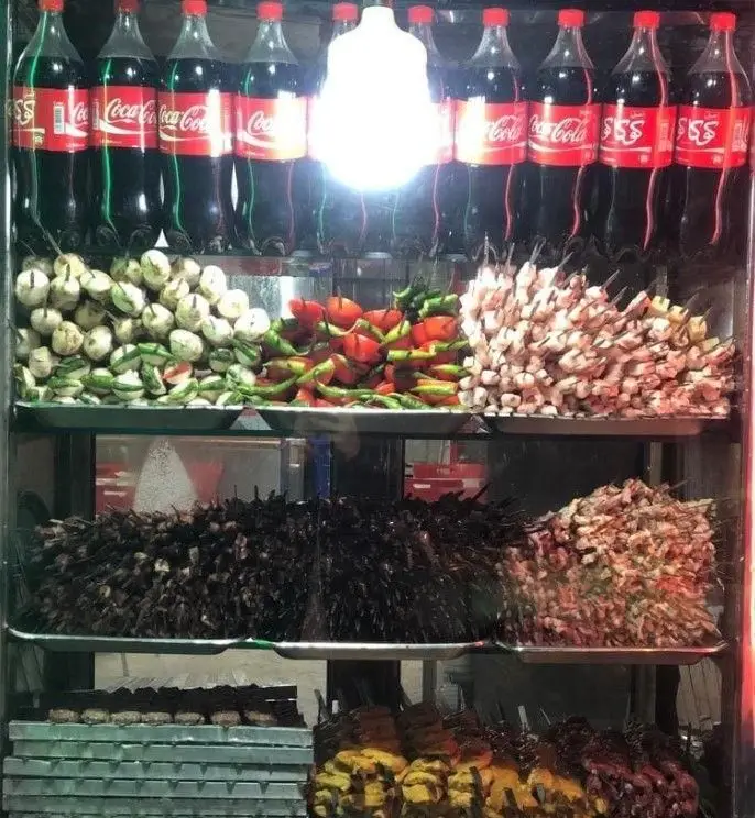 تصویر ویترین جگرسرای ستارخان با انواع کباب سیخی تازه: جگر، دل، قلوه، جوجه، و سبزیجات آماده طبخ و سرو.