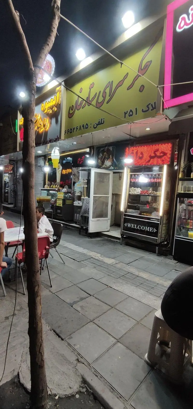 نمایی شبانه از جگرسرای ستارخان، ارائه دهنده انواع جگر داغ، آبمیوه تازه، بستنی و معجون، با محیطی پر جنب و جوش برای مشتریان