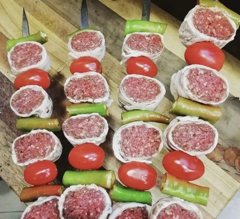 آماده‌سازی کباب‌های لذیذ جگرسرای ستارخان: سیخ‌های گوشت تازه کوبیده، گوجه و فلفل سبز، آماده برای کبابی بی‌نظیر.